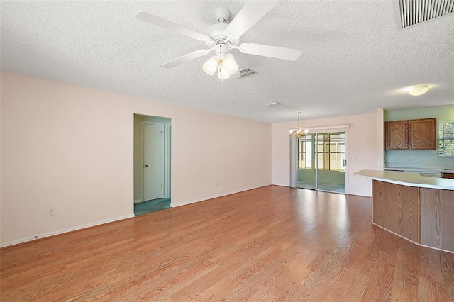 unfurnished living room featuring a textured ceiling, ceiling fan with notable chandelier, and light wood-type flooring