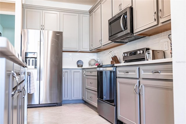 kitchen with appliances with stainless steel finishes, light tile patterned floors, gray cabinets, and tasteful backsplash