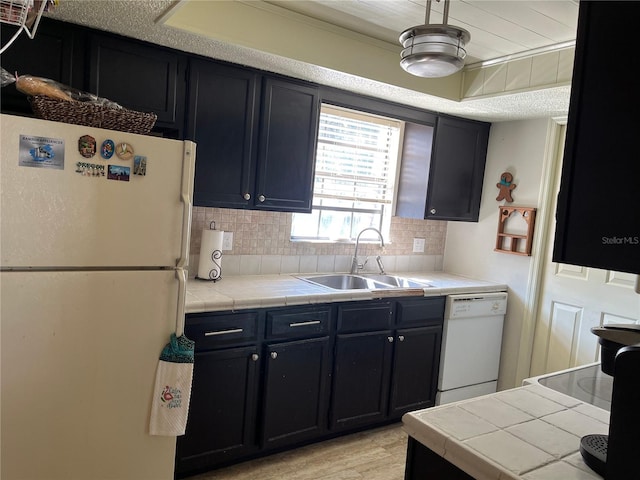 kitchen featuring sink, white appliances, tasteful backsplash, tile counters, and light wood-type flooring