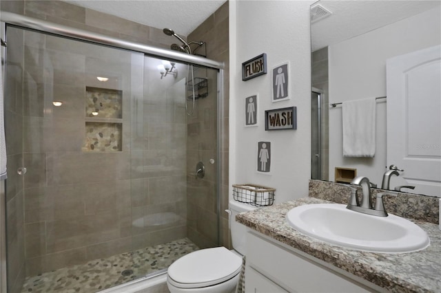 bathroom with a textured ceiling, vanity, toilet, and a shower with shower door