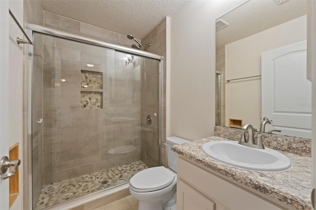 bathroom with a textured ceiling, toilet, visible vents, vanity, and a stall shower