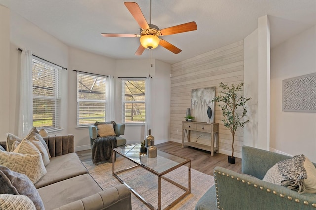 living room with a ceiling fan, wooden walls, baseboards, and wood finished floors