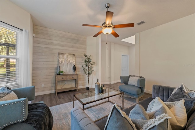 living room with baseboards, visible vents, ceiling fan, wood finished floors, and wood walls