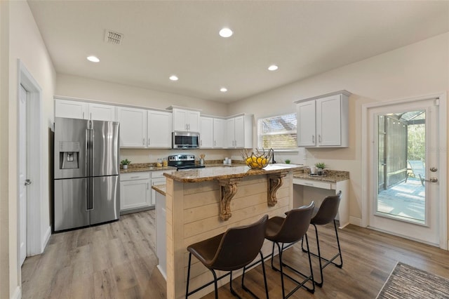 kitchen featuring visible vents, appliances with stainless steel finishes, light stone countertops, light wood-type flooring, and a kitchen bar