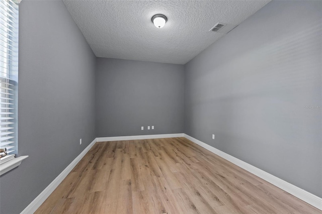 spare room with visible vents, light wood finished floors, baseboards, and a textured ceiling