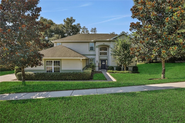 traditional home with a shingled roof, a front yard, and stucco siding