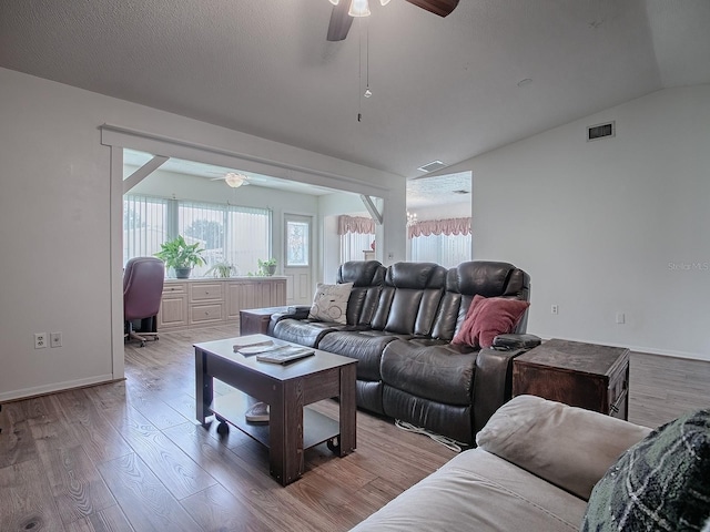 living room with light wood-type flooring, vaulted ceiling, ceiling fan, and a textured ceiling