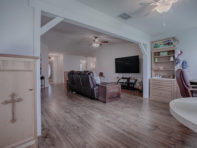 living room with light hardwood / wood-style flooring, vaulted ceiling, ceiling fan, and a textured ceiling