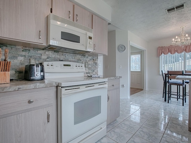 kitchen featuring white appliances, a textured ceiling, light brown cabinetry, and a chandelier