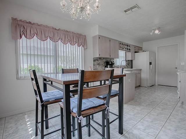 dining area with a textured ceiling, light tile patterned floors, sink, and a chandelier