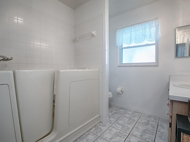 bathroom with a textured ceiling, tiled shower, vanity, and toilet