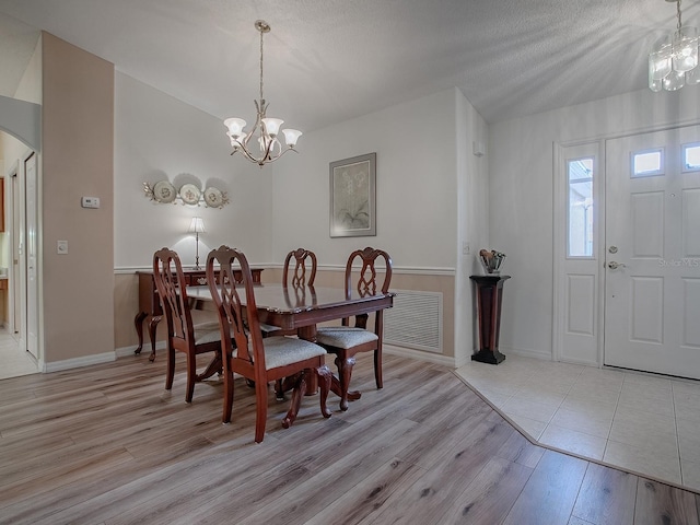 dining area with a notable chandelier, light wood-type flooring, and a textured ceiling