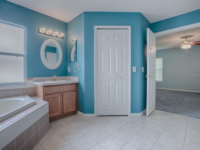 bathroom with ceiling fan, vanity, a textured ceiling, tiled bath, and tile patterned flooring