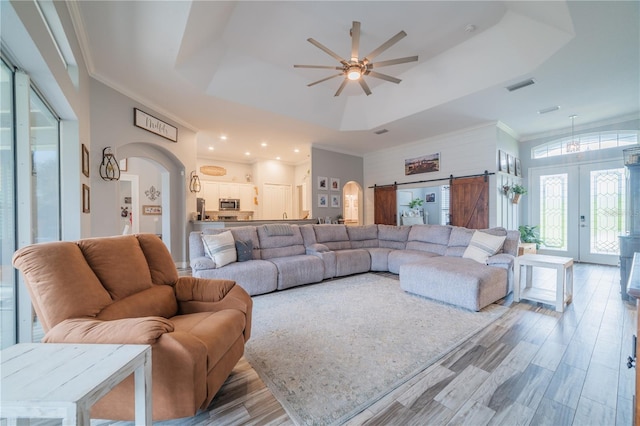 living room with a barn door, a tray ceiling, ceiling fan, ornamental molding, and hardwood / wood-style floors