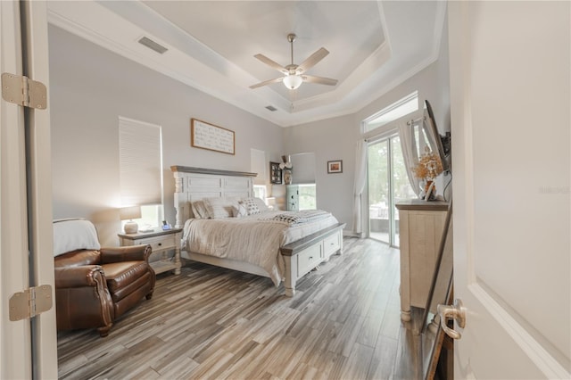 bedroom featuring ceiling fan, a raised ceiling, light hardwood / wood-style flooring, crown molding, and access to exterior