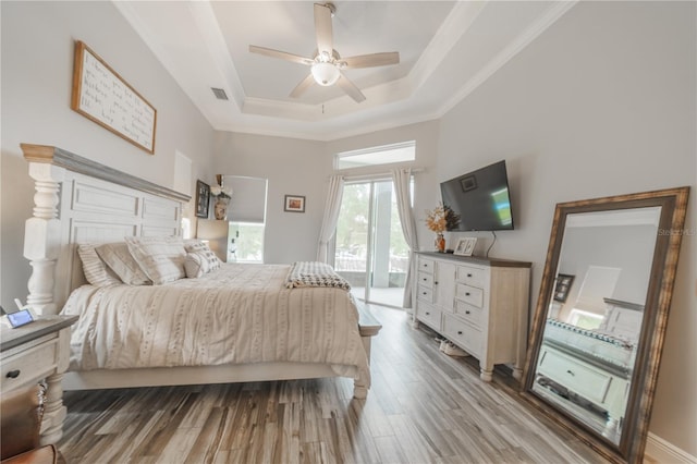 bedroom featuring light hardwood / wood-style flooring, a tray ceiling, ceiling fan, and access to exterior