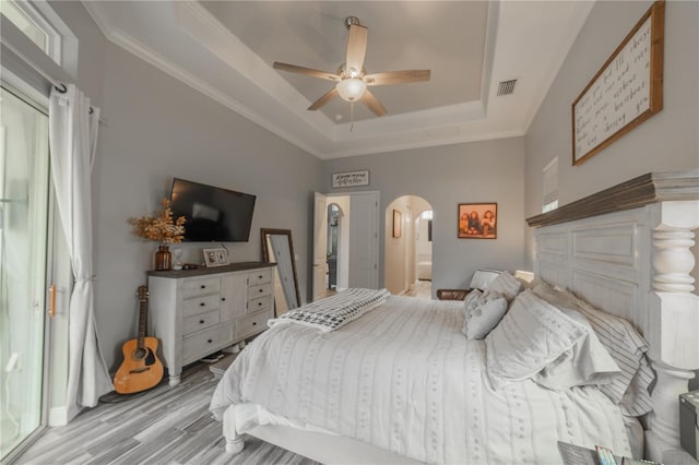 bedroom with ceiling fan, a raised ceiling, light wood-type flooring, and ornamental molding