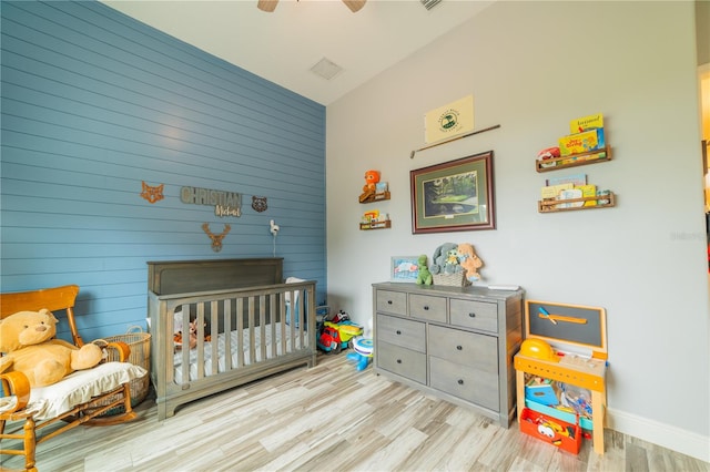 bedroom featuring a crib, light wood-type flooring, and ceiling fan