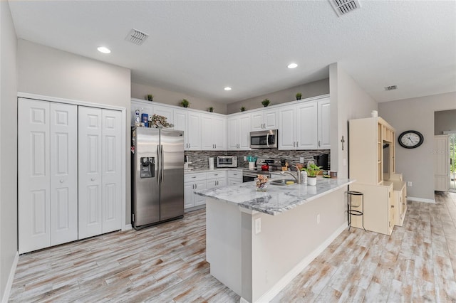 kitchen with appliances with stainless steel finishes, white cabinetry, light stone counters, kitchen peninsula, and light hardwood / wood-style flooring