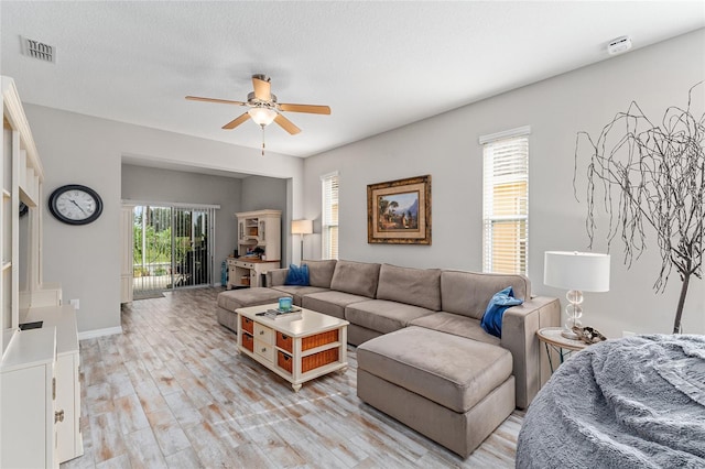 living room with ceiling fan, a textured ceiling, and light wood-type flooring