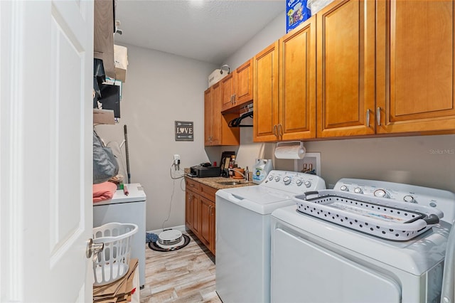 laundry area featuring sink, washing machine and clothes dryer, a textured ceiling, light hardwood / wood-style flooring, and cabinets