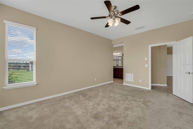 unfurnished bedroom featuring ceiling fan, light colored carpet, and ensuite bath