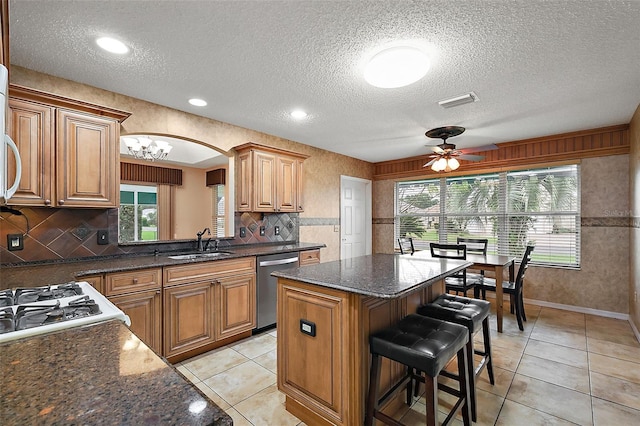 kitchen featuring sink, dishwasher, a kitchen island, ceiling fan with notable chandelier, and a textured ceiling