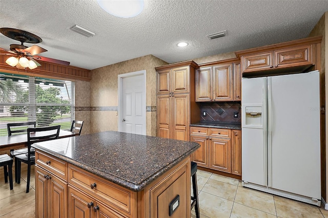 kitchen with light tile patterned flooring, a textured ceiling, a center island, white refrigerator with ice dispenser, and ceiling fan