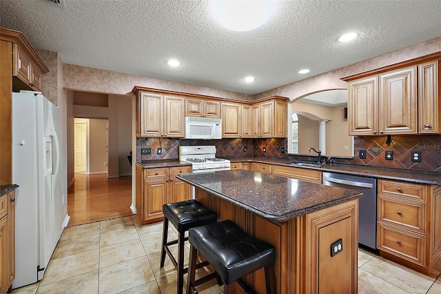 kitchen with white appliances, sink, a kitchen bar, a textured ceiling, and a center island