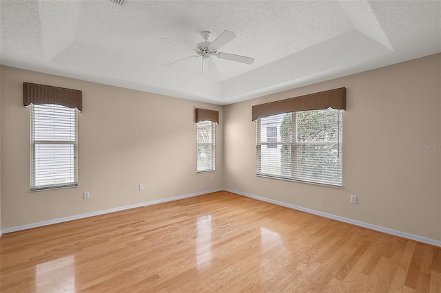 unfurnished room featuring ceiling fan, a raised ceiling, a textured ceiling, and light hardwood / wood-style flooring