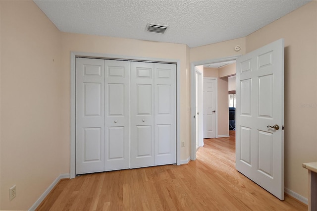 unfurnished bedroom featuring a closet, a textured ceiling, and light hardwood / wood-style flooring