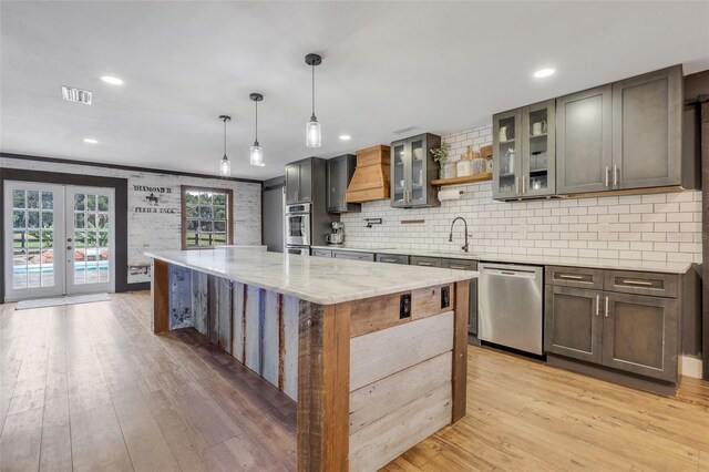 kitchen with hanging light fixtures, a kitchen island, light hardwood / wood-style flooring, dishwasher, and light stone countertops