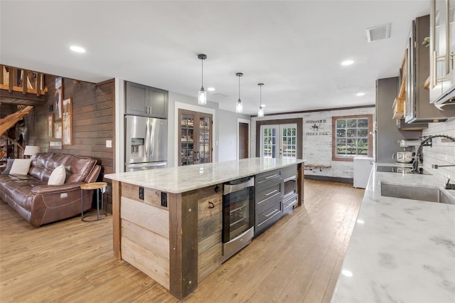 kitchen with wine cooler, hanging light fixtures, sink, stainless steel fridge with ice dispenser, and light stone countertops