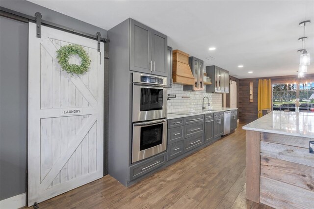 kitchen with appliances with stainless steel finishes, hanging light fixtures, a barn door, and gray cabinetry