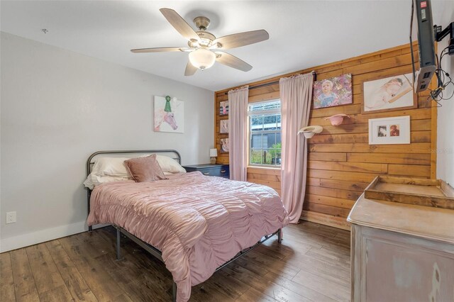 bedroom with wood walls, ceiling fan, and dark wood-type flooring