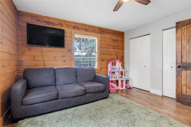 living room with ceiling fan, wooden walls, and hardwood / wood-style floors