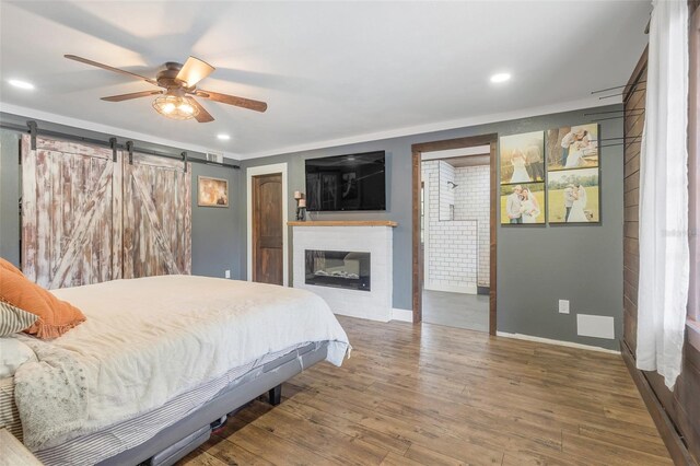 bedroom featuring ceiling fan, hardwood / wood-style flooring, a fireplace, and a barn door