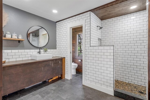 bathroom with a tile shower, tile walls, tile patterned flooring, vanity, and toilet