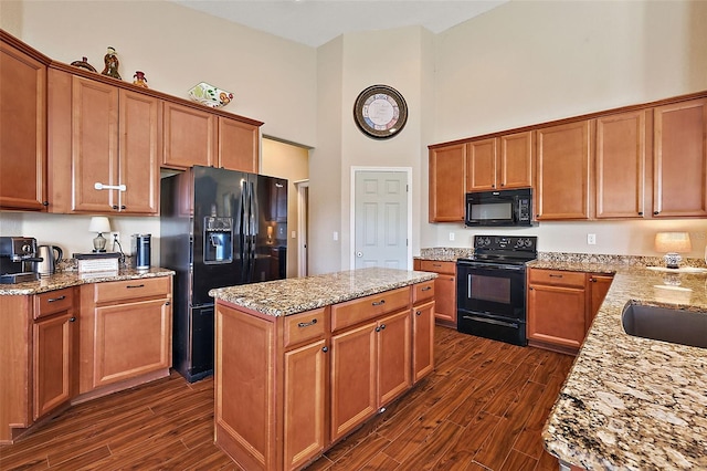 kitchen with a high ceiling, light stone counters, dark hardwood / wood-style floors, and black appliances