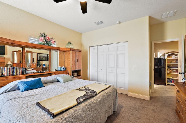 carpeted bedroom with ceiling fan, black fridge, a textured ceiling, and a closet