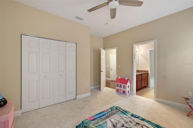 bedroom featuring a closet, light colored carpet, ceiling fan, and ensuite bath