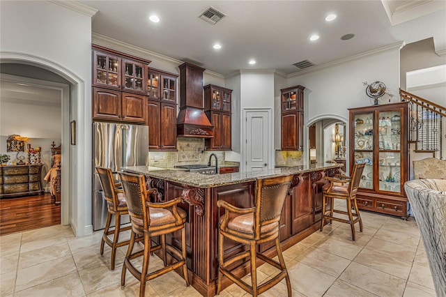 kitchen featuring premium range hood, crown molding, stainless steel fridge with ice dispenser, and light stone counters