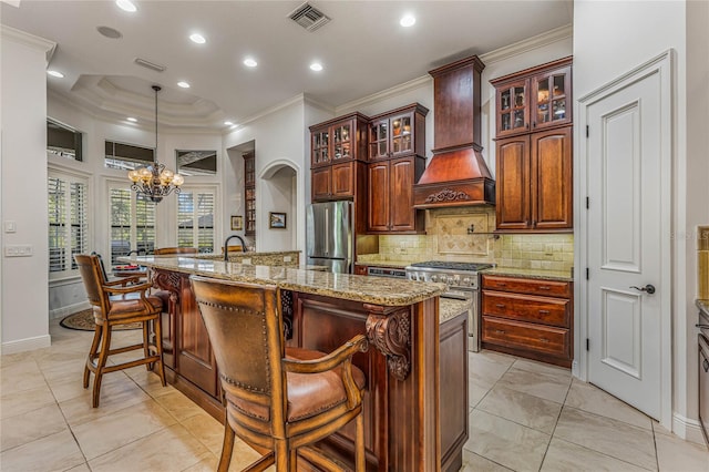 kitchen featuring appliances with stainless steel finishes, premium range hood, pendant lighting, an inviting chandelier, and a center island with sink