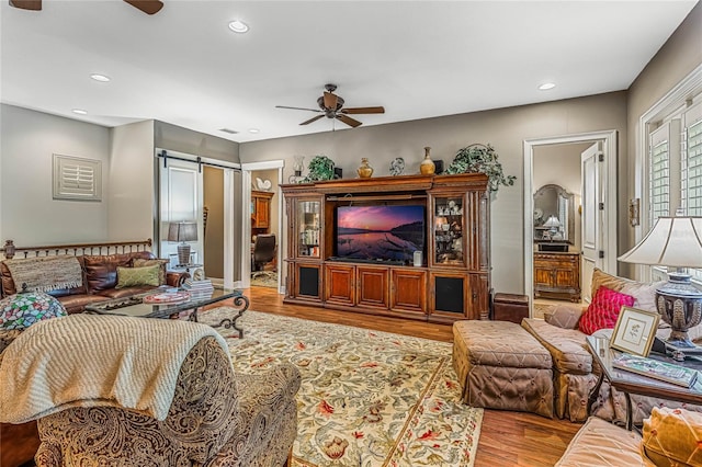 living room with a barn door, light wood-type flooring, and ceiling fan