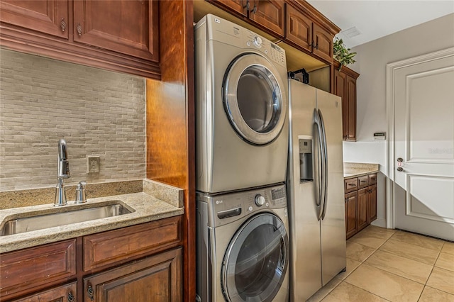 clothes washing area with cabinets, stacked washer / drying machine, light tile patterned flooring, and sink