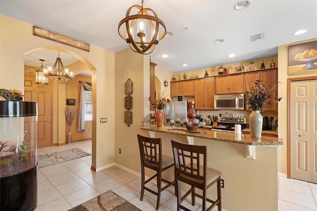 kitchen featuring hanging light fixtures, light tile patterned floors, kitchen peninsula, stainless steel appliances, and dark stone countertops