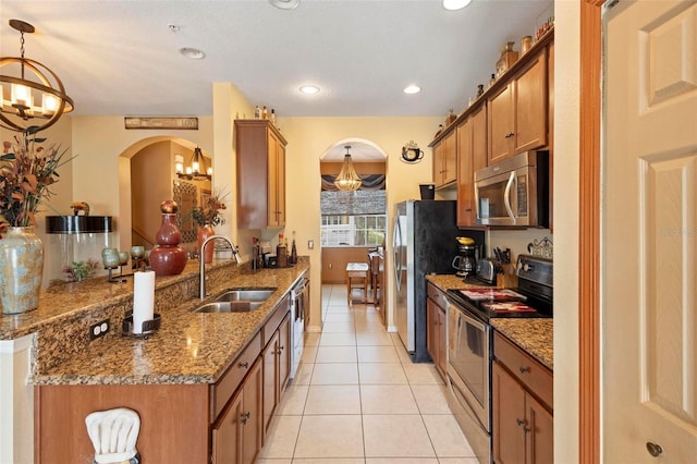 kitchen featuring sink, kitchen peninsula, appliances with stainless steel finishes, decorative light fixtures, and dark stone countertops