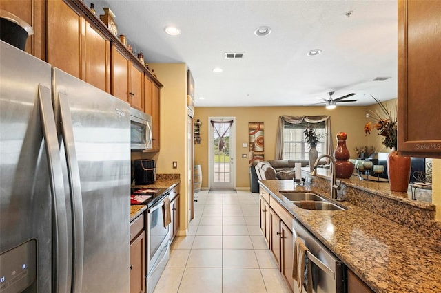 kitchen featuring appliances with stainless steel finishes, dark stone countertops, light tile patterned floors, ceiling fan, and sink