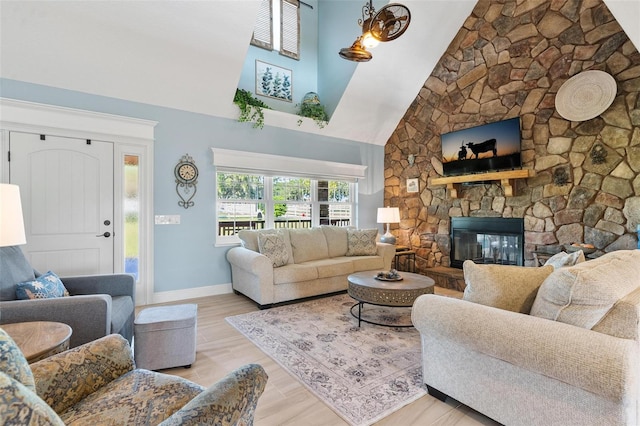 living room featuring high vaulted ceiling, light hardwood / wood-style flooring, and a stone fireplace