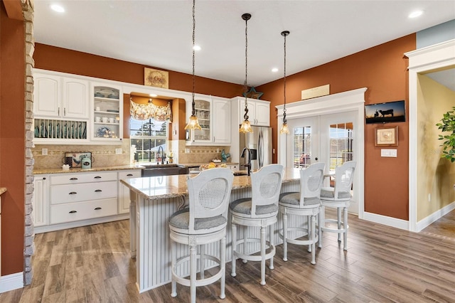 kitchen with stainless steel fridge, an island with sink, white cabinetry, plenty of natural light, and light stone counters